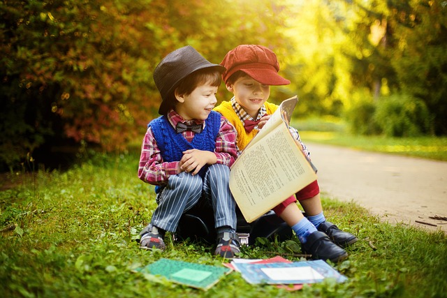 Two small boys reading books in a park