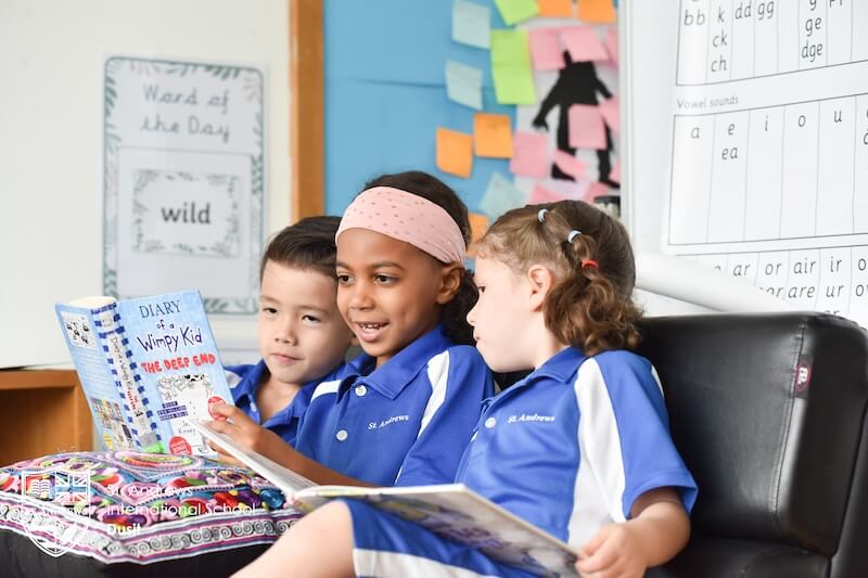 3 school kids reading a book in a classroom 